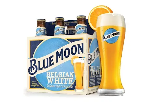 Six-pack of Blue Moon Belgian White beer bottles with a poured glass garnished with an orange slice, displayed against a clean white background.