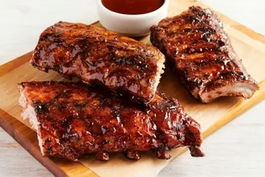 Baby Back Ribs Party Platter featuring glazed, slow-cooked barbecue ribs served on a wooden board with a side of barbecue dipping sauce.