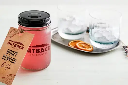 Blueberry Lavender Lemonade for Two served in a mason jar with an Outback Steakhouse label, accompanied by glasses with ice and dried citrus slices on a tray