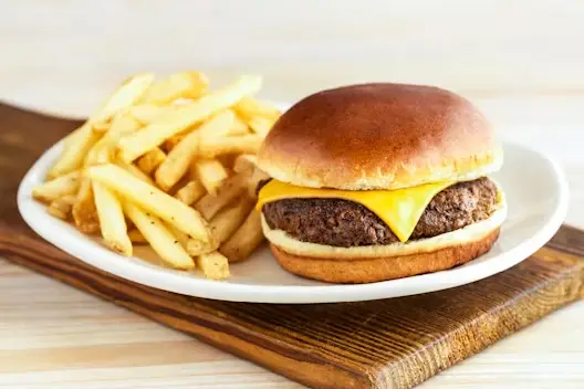 Boomerang Cheeseburger with a juicy beef patty topped with melted cheddar cheese, served with a side of seasoned French fries on a white plate.