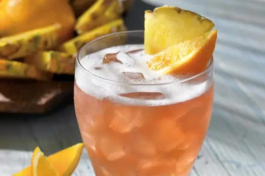 Refreshing Castaway Cocktail garnished with pineapple and orange slices served over ice in a chilled glass.