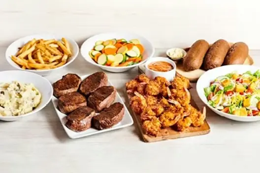 Center-Cut Sirloin & Coconut Shrimp for 6 featuring seasoned sirloin steaks and crispy coconut shrimp served with French fries, mashed potatoes, mixed vegetables, fresh garden salad, and dinner rolls with butter on a light wooden table.