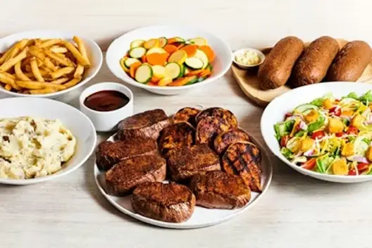 Center-Cut Sirloin & Grilled Chicken for 6 featuring seasoned sirloin steaks and grilled chicken breasts, served with French fries, mashed potatoes, mixed vegetables, fresh garden salad, and bread with butter on a light wooden table.