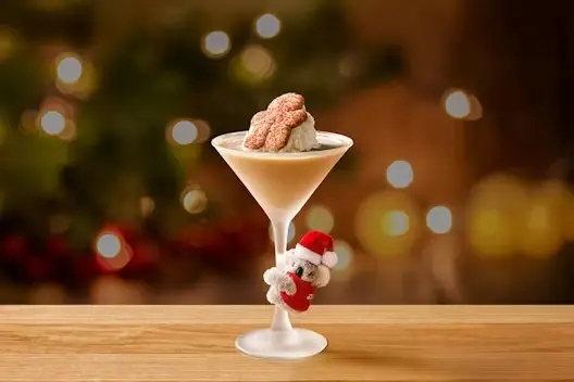 Festive Gingerbread Cookie Martini topped with whipped cream and gingerbread cookies in a martini glass, with a small Santa koala ornament and warm holiday lights in the background.