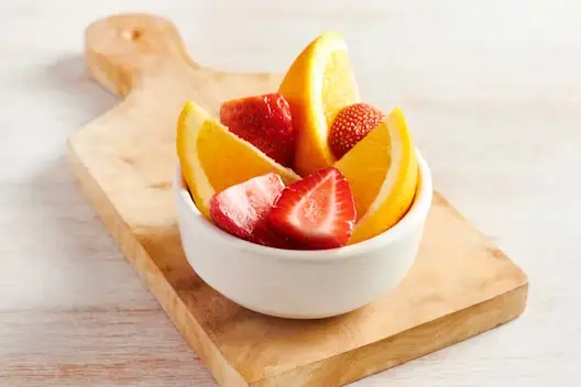 Kids Fruit bowl filled with fresh orange slices and strawberries, served in a white dish placed on a wooden board.