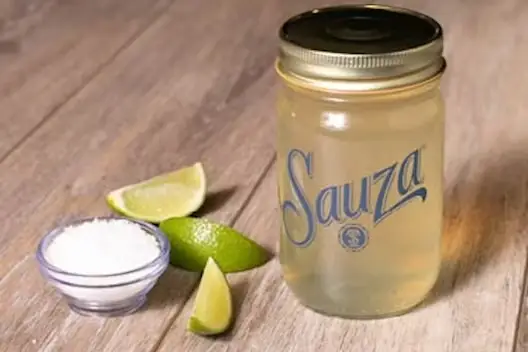 Sauza Gold Coast ‘Rita for Two in a mason jar with lime wedges and salt on a wooden table.