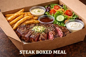 Steak Boxed Meal featuring sliced grilled steak topped with garlic butter, served with seasoned fries, fresh garden salad, and dipping sauces