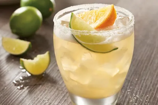 Refreshing Top Shelf Rita margarita served over ice with lime and orange garnish and a salted rim.